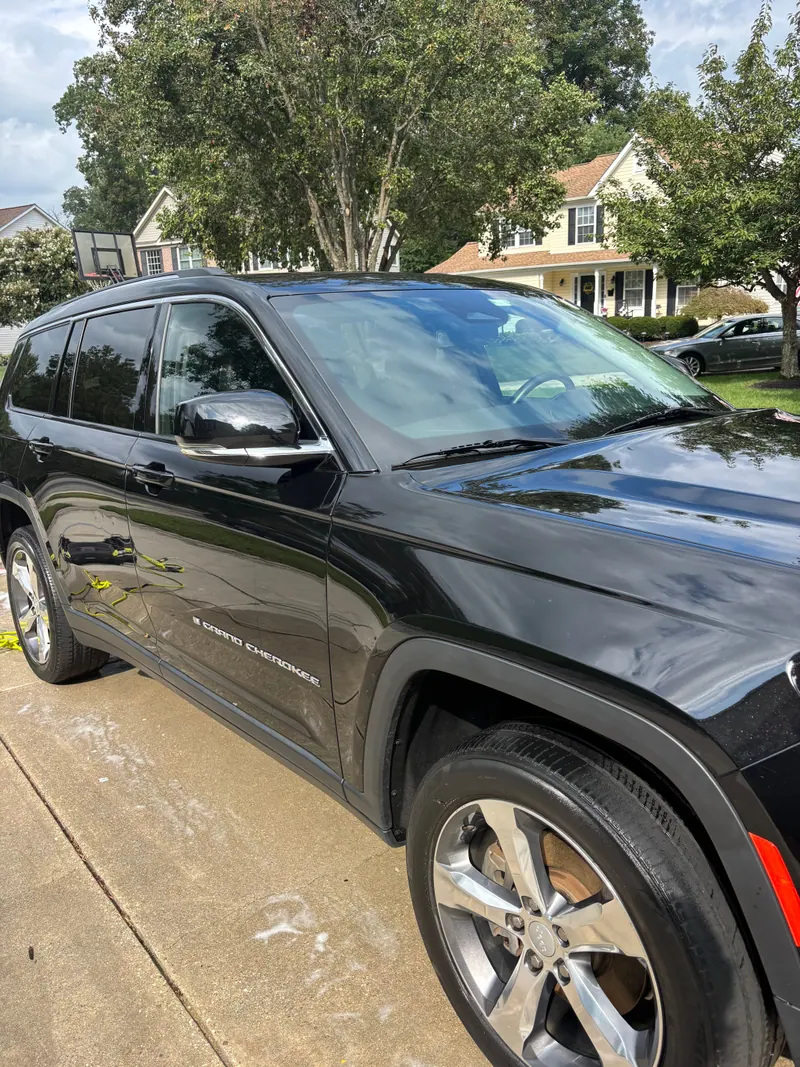 Black Jeep Grand Cherokee L in profile on a driveway, paint and chrome gleaming