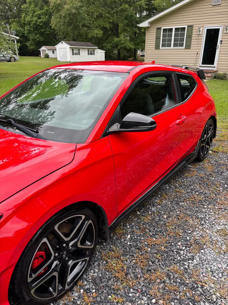 Red Hyundai Veloster in profile on gravel, paint polished and wheels cleaned